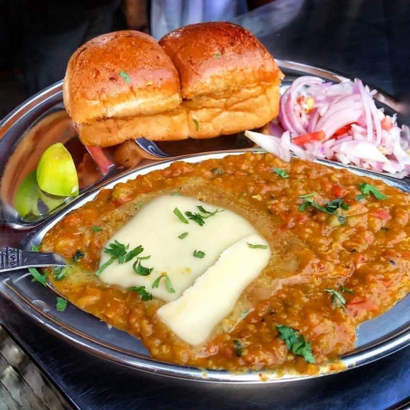 Pav Bhajji consists of a thick vegetable curry served with a soft bread roll. It is essentially a spiced mixture of mashed potatoes in a thick gravy, usually cooked on a flat griddle and served hot with a soft white bread roll.